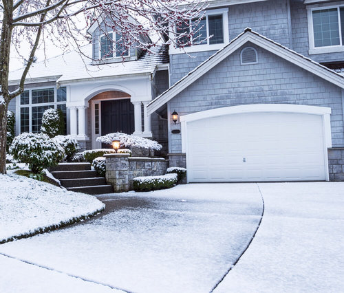Beautiful home in winter with snow garage bushes and lighting