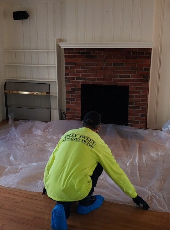 Safety Measures - Drop Cloths tech in yellow Billy Sweet shirt and blue covers on shoes in front of brick fireplace